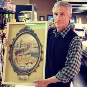 Mike Pronio holds a large framed picture of a deer in the winter.