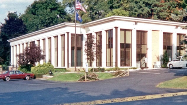 A two-story white building with windows reaching from the ground to the roof. A parking lot with retro cars.