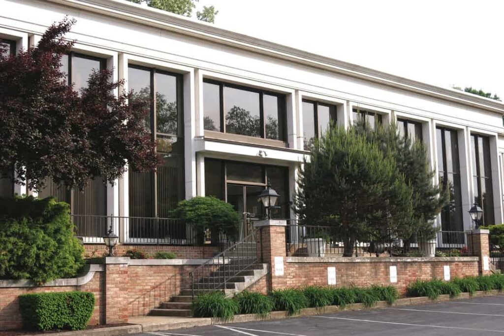 The front facade of a building with a brick staircase leading up to white walls with floor to ceiling windows.